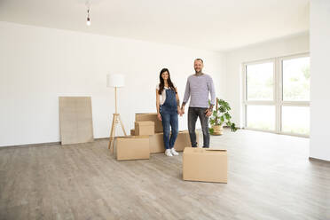 Couple with cardboard boxes and electric lamp standing in new home - MJFKF00552