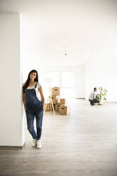 Pregnant woman standing by wall while husband arranging monstera in new home - MJFKF00557