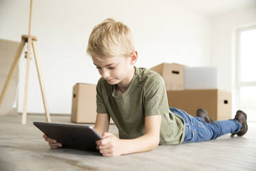 Boy with blond hair using digital tablet while lying on floor in new house - MJFKF00582