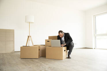 Businessman using laptop on cardboard box while working from new home - MJFKF00584