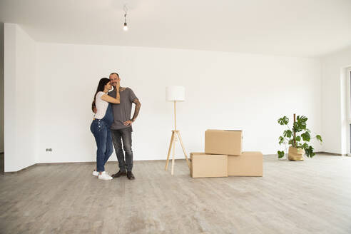 Romantic couple standing by electric lamp and boxes standing against wall in new apartment - MJFKF00627