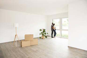Couple looking through window while standing in new unfurnished home - MJFKF00628