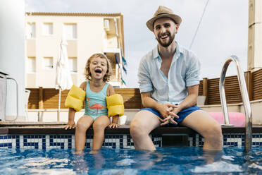 Laughing girl with her uncle sitting on poolside - JRFF04693