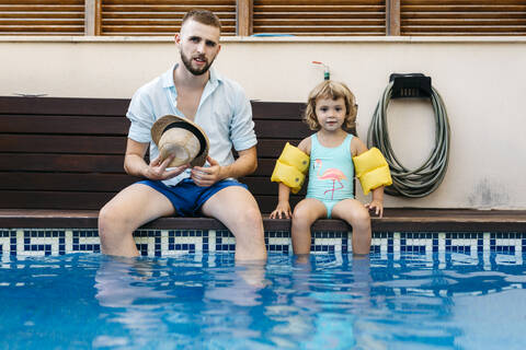 Little girl with her uncle sitting on poolside stock photo
