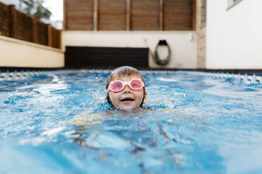 Little girl with swimming goggles in swimming pool - JRFF04702