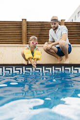 Little girl jumping into water, her uncle at poolside - JRFF04707