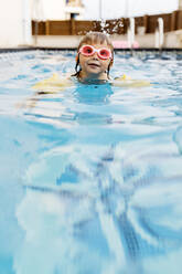 Little girl with swimming goggles in swimming pool - JRFF04713