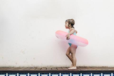 Little girl with floating tire walking at pool edge stock photo