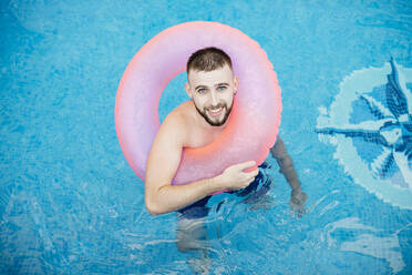 Junger lächelnder Mann mit rosa Schwimmreifen im Pool - JRFF04721