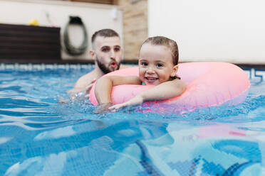 Little girl with floating tire and her uncle in swimming pool - JRFF04724