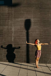 Dancing young woman casting shade on black wall at sunset - TCEF00986