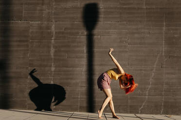 Tanzende junge Frau, die bei Sonnenuntergang Schatten auf eine schwarze Wand wirft - TCEF00988