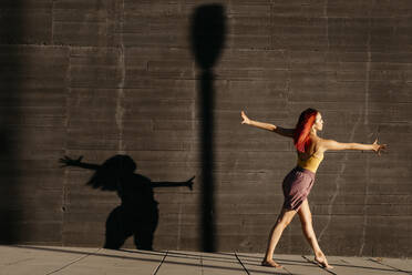 Dancing young woman casting shade on black wall at sunset - TCEF00989