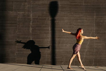 Tanzende junge Frau, die bei Sonnenuntergang Schatten auf eine schwarze Wand wirft - TCEF00989