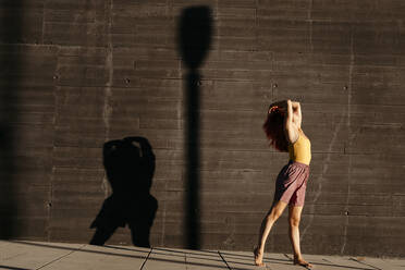 Dancing young woman casting shade on black wall at sunset - TCEF00990