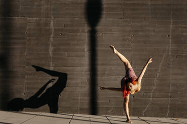 Dancing young woman casting shade on black wall at sunset - TCEF00991