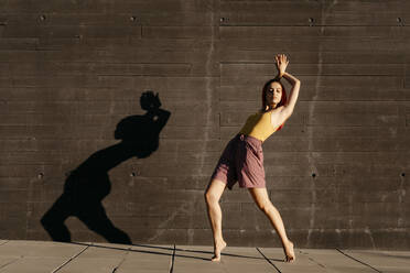 Dancing young woman casting shade on black wall at sunset - TCEF00992