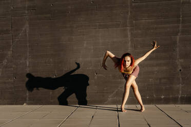 Tanzende junge Frau, die bei Sonnenuntergang Schatten auf eine schwarze Wand wirft - TCEF00993