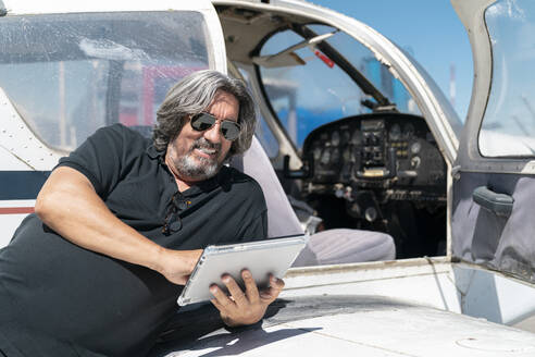 Mechaniker lehnt sich an ein Flugzeug und benutzt ein digitales Tablet - MTBF00639