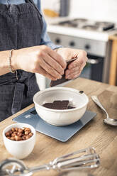 Frau wiegt Schokoladenriegel, während sie in der Küche zu Hause steht - MSUF00296
