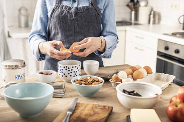 Frau mit Schürze schlägt ein Ei auf, um einen Kuchen zu Hause zu backen - MSUF00302