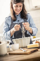 Lächelnde Frau, die einen Schneebesen benutzt, während sie in der Küche zu Hause steht - MSUF00309