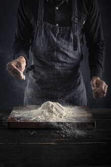 Bäcker streut Mehl, während er am Tisch steht - MSUF00314