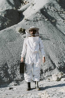 Mann mit Aktentasche in Imkerkleid in einer trockenen apokalyptischen Landschaft - AFVF07090