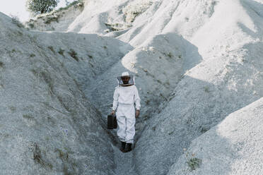 Mann mit Aktentasche in Imkerkleid in einer trockenen apokalyptischen Landschaft - AFVF07094