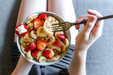 Hände eines Teenagers, der eine Schüssel mit Mini-Pfannkuchen mit Erdbeeren und Bananen isst - SARF04622