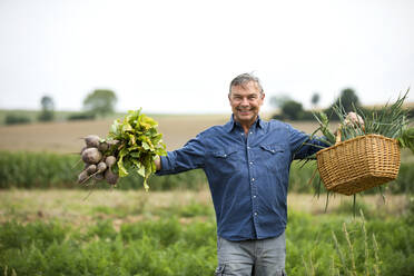 Ein Mann lächelt, während er auf einem Bauernhof Gemüse in beiden Händen hält - MAEF13008