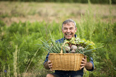 Mann hält Gemüsekorb, während er auf dem Bauernhof sitzt - MAEF13009