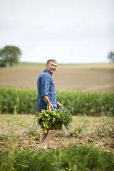 Glücklicher Bauer hält Gemüsekorb beim Spaziergang auf dem Bauernhof - MAEF13012