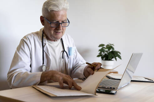 Leitender Arzt, der in der Klinik sitzend die Krankenakte betrachtet - AFVF07109