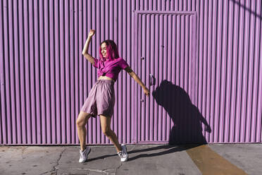 Young woman with dyed red hair dancing in front of purple wall in the city - TCEF00994