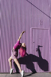 Young woman with dyed red hair dancing in front of purple wall in the city - TCEF00996