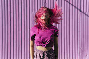 Young woman with dyed red hair dancing in front of purple wall in the city - TCEF00997