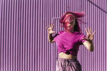 Young woman with dyed red hair dancing in front of purple wall in the city - TCEF00998