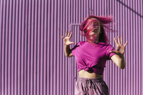 Junge Frau mit gefärbten roten Haaren tanzt vor einer lila Wand in der Stadt - TCEF00998