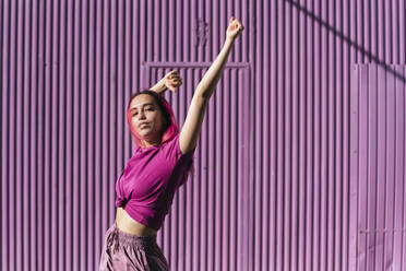 Young woman with dyed red hair dancing in front of purple wall in the city - TCEF00999