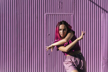 Young woman with dyed red hair dancing in front of purple wall in the city - TCEF01000