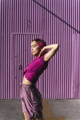 Junge Frau mit gefärbten roten Haaren tanzt vor einer lila Wand in der Stadt - TCEF01001