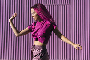 Junge Frau mit gefärbten roten Haaren tanzt vor einer lila Wand in der Stadt - TCEF01002