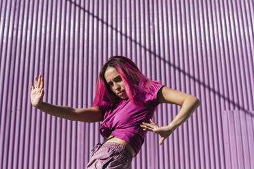 Young woman with dyed red hair dancing in front of purple wall in the city - TCEF01003