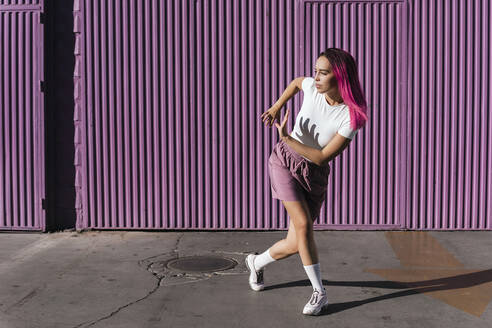 Junge Frau mit gefärbten roten Haaren tanzt vor einer lila Wand in der Stadt - TCEF01006