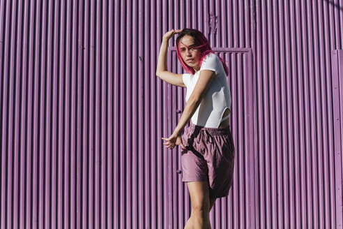 Young woman with dyed red hair dancing in front of purple wall in the city - TCEF01007