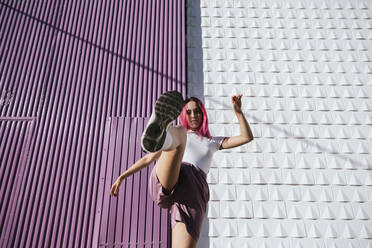 Young woman with dyed red hair dancing in front of purple wall in the city - TCEF01017