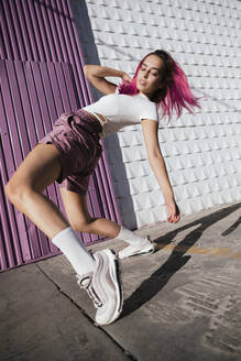 Young woman with dyed red hair dancing in front of purple wall in the city - TCEF01018