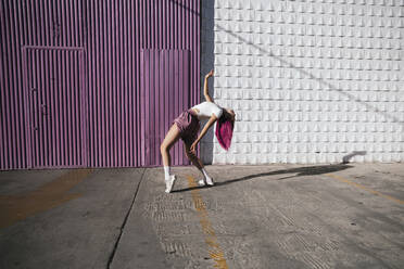 Young woman with dyed red hair dancing in front of purple wall in the city - TCEF01020