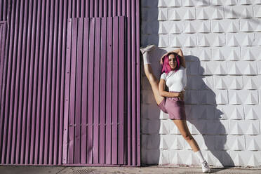 Young woman performing standing splits against purple wall - TCEF01021